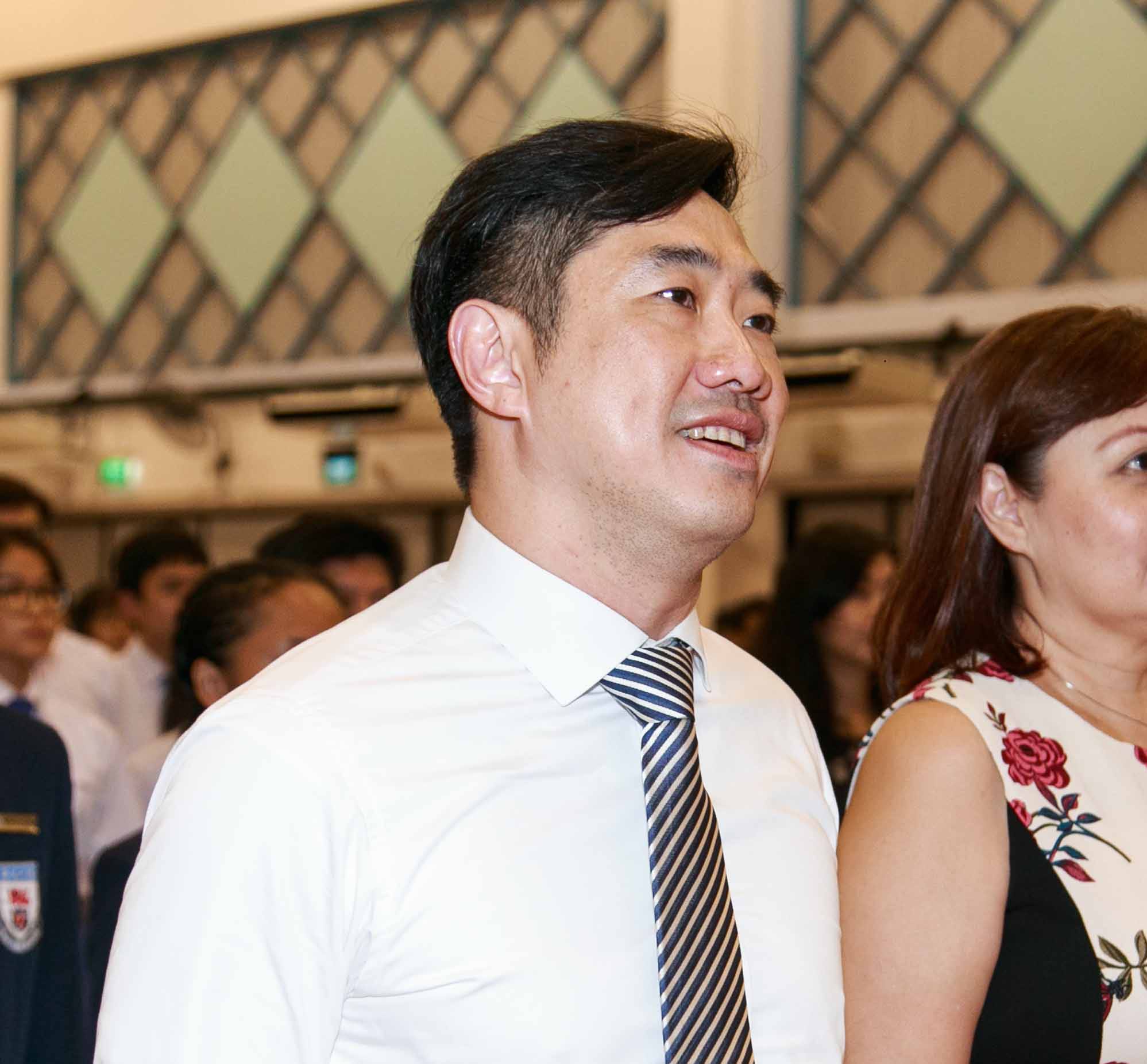 A man in a white shirt and striped tie smiles and looks upward, with a woman in a floral dress beside him.